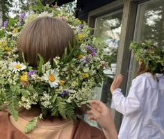 a woman with flowers on her head standing in front of a window and another person behind her