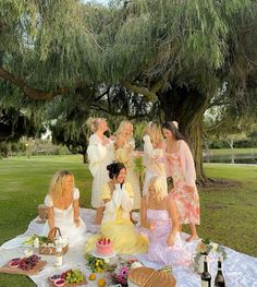 a group of women sitting on top of a picnic blanket next to a large tree