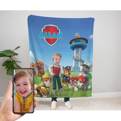 a child holding up a phone with a paw patrol photo on the screen and an image of a boy in yellow shirt