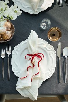 a table set with white plates and silverware, napkins and flowers on it