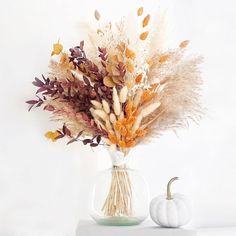 a vase filled with dried flowers next to a white pumpkin