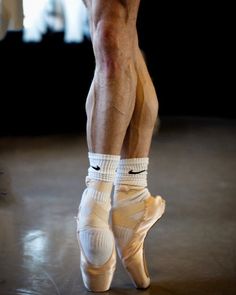 the legs and ankles of a ballerina in white ballet shoes, with socks on