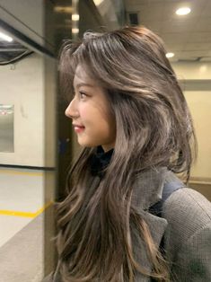 a woman with long brown hair standing in front of a train door and looking off into the distance