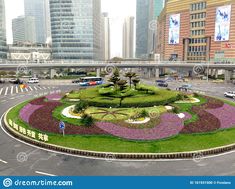 a circular flower bed in the middle of a city street with tall buildings behind it