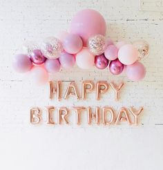 a happy birthday sign surrounded by balloons and confetti on a white brick wall