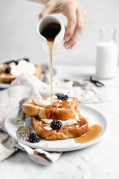 a person pouring syrup onto a stack of waffles on a plate with berries