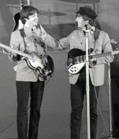 two men standing next to each other while holding guitars and singing into the microphones