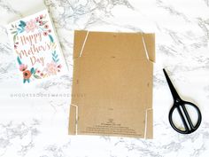 a pair of scissors sitting on top of a card next to a box with a happy mother's day greeting