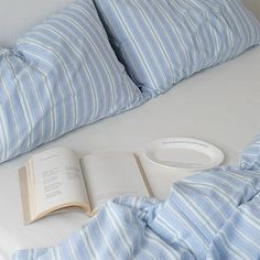 an open book on a bed with blue and white striped sheets, pillows and pillow cases