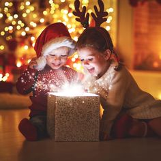 two young children are playing with a small box on the floor in front of christmas lights