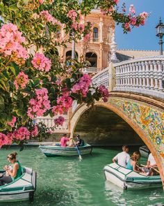 people are floating on boats in the water near a bridge with flowers hanging over it