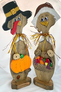 two wooden scarecrows holding pumpkins and squash