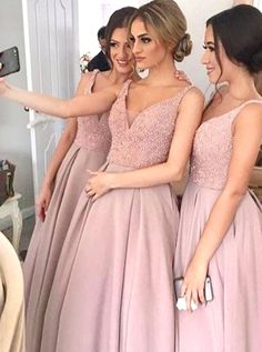 two women in dresses taking a selfie with their cell phone while another woman takes a photo