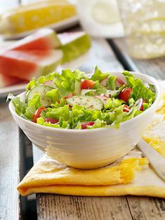 a salad with cucumbers, tomatoes and lettuce in a white bowl