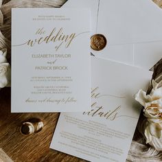 the wedding stationery is laid out on a wooden table with flowers and rings around it