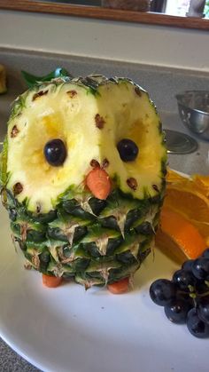 a pineapple shaped like an owl sitting on top of a plate next to grapes and cheese