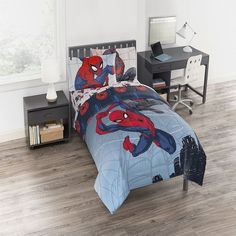 a bed with spiderman comforter and sheets on it in a room next to a desk