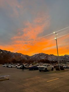 a parking lot filled with lots of parked cars under a sunset colored sky and mountains