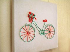 a white wall hanging with a red and green embroidered bicycle on it's side