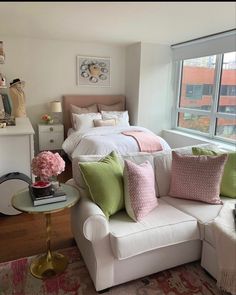 a bedroom with a white couch, pink and green pillows, and a large window