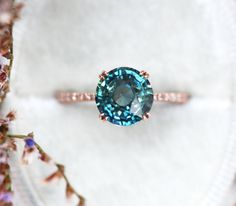 a blue diamond ring sitting on top of a white cloth next to some pink flowers