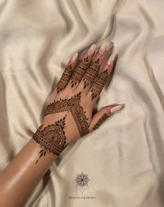 a woman's hand with henna on top of white sheets and satin material