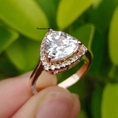 a close up of a person's hand holding a ring with a pear shaped diamond