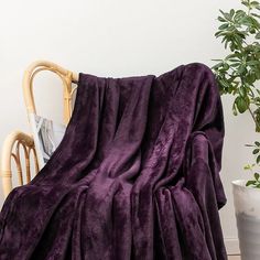 a purple blanket sitting on top of a chair next to a potted plant