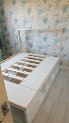 a bed frame with drawers underneath it in a room that has floral wallpaper on the walls