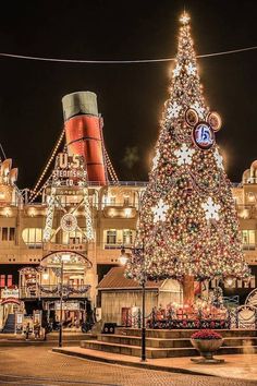 a large christmas tree is lit up in front of a building with lights on it