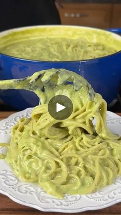 a bowl of green pasta with a spoon in it on a table next to a blue bowl