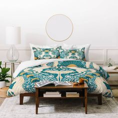 a bed with blue and yellow comforters in a room next to a table, lamp and potted plant