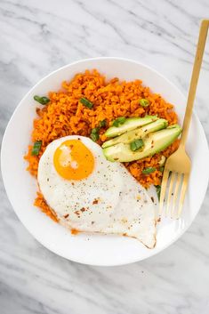 a white plate topped with rice and an egg next to avocado wedges