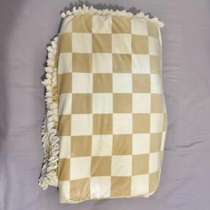 a brown and white checkered blanket laying on top of a purple bed sheet with tassels