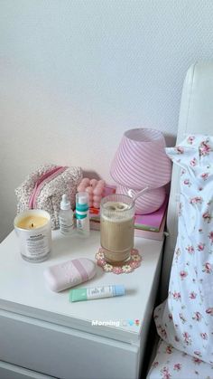 a white table topped with lots of different items next to a pink lamp and pillow