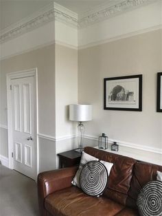 a brown leather couch sitting in a living room next to a lamp and pictures on the wall