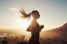 a woman running in the sun with her hair blowing in the wind while looking out over a city