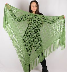 a woman holding up a green crocheted shawl