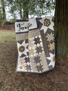 a quilt hanging from the side of a tree in front of a sign that says, farm