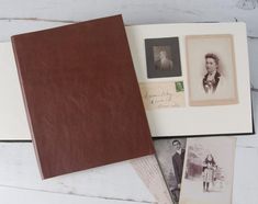 an open book with photos on it sitting on a white table next to other items