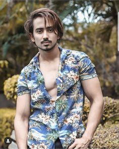 a man with no shirt on standing in front of some rocks and trees, posing for the camera