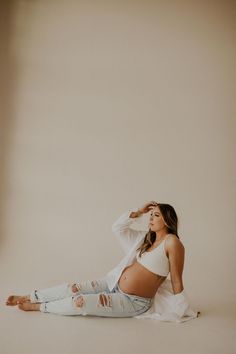 a pregnant woman sitting on the floor with her hands behind her head and looking up