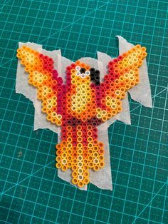 a bird made out of perler beads sitting on top of a piece of paper