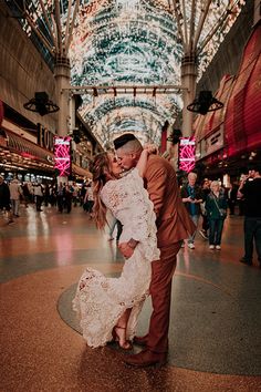 a man and woman are kissing in an indoor shopping mall with christmas lights on the ceiling