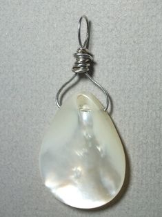 Mother of Pearl Bead Pendant Wire Wrapped in .925 Sterling Silver Round Wire This refreshing and enlightening mother of pearl bead displays a fine fluid silver-white to iridescent (pearlescent) sheen. Versatile, it wears well with almost any color of clothing, including both gray and brown based color tones. It gives a sharp contrast to darker colors and a pleasant blend to lighter/pastel colors. It is also a nice match with most earth tone colors. Consistent color and teardrop shape give some a White Shell-shaped Pearl Drop Necklace, Silver Mother Of Pearl Shell Jewelry, Oval White Wire Wrapped Jewelry, White Shell-shaped Jewelry With Pearl Pendant, Pearl White Drop Jewelry With High Luster, Silver Pearl Pendant Jewelry In Mother Of Pearl, Teardrop High Luster Pearl Necklace For Gift, Iridescent Pearl Jewelry With Pearl Drop, Pearl White High Luster Teardrop Jewelry