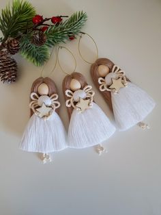 three little angel ornaments are hanging on the wall next to pine cones and evergreen branches