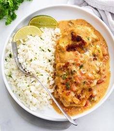 a white plate topped with rice and meat covered in gravy next to a lime wedge