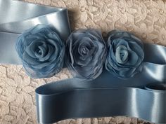 three large blue flowers on a silver satin ribbon with two matching sashes attached to it