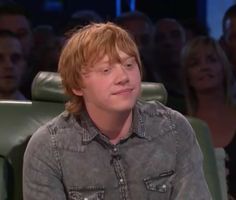 a young man sitting in front of a group of people on a tv show, looking at the camera