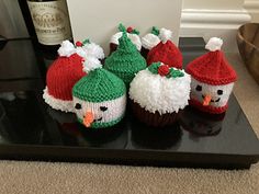 knitted christmas cupcakes with santa hats and snowmen are on a tray next to a bottle of wine